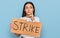 Young hispanic girl holding strike banner cardboard serious face thinking about question with hand on chin, thoughtful about