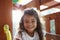 Young Hispanic girl playing on a climbing frame in a playground smiling to camera, backlit, close up