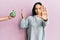 Young hispanic girl rejecting jar of pills with hand with open hand doing stop sign with serious and confident expression, defense