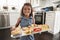 Young Hispanic girl standing in kitchen presenting cakes she’s baked and smiling to camera