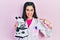 Young hispanic girl wearing scientist uniform holding microscope pointing finger to one self smiling happy and proud