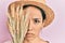 Young hispanic girl wearing summer hat holding spike wheat over eye depressed and worry for distress, crying angry and afraid