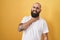 Young hispanic man with beard and tattoos standing over yellow background touching painful neck, sore throat for flu, clod and