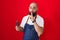 Young hispanic man with beard and tattoos wearing barber apron holding razor asking to be quiet with finger on lips