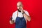 Young hispanic man with beard and tattoos wearing barber apron holding razor mouth and lips shut as zip with fingers