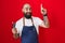 Young hispanic man with beard and tattoos wearing barber apron holding razor pointing finger up with successful idea