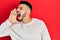 Young hispanic man with beard wearing casual winter sweater shouting and screaming loud to side with hand on mouth