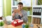 Young hispanic man business worker unpacking gift holding letter at office