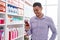 Young hispanic man customer smiling confident using smartphone at pharmacy