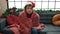 Young hispanic man feeling cold covered with blanket sitting on sofa by christmas decoration at home