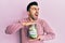 Young hispanic man holding charity jar with money angry and mad screaming frustrated and furious, shouting with anger