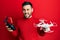 Young hispanic man holding drone and remote control with smartphone winking looking at the camera with sexy expression, cheerful