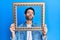 Young hispanic man holding empty frame looking at the camera blowing a kiss being lovely and sexy