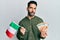 Young hispanic man holding italy flag and euros banknotes making fish face with mouth and squinting eyes, crazy and comical