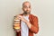 Young hispanic man holding pile of tasty colorful doughnuts puffing cheeks with funny face