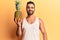 Young hispanic man holding pineapple looking positive and happy standing and smiling with a confident smile showing teeth