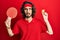 Young hispanic man holding red ping pong racket and ball clueless and confused expression