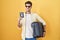 Young hispanic man holding suitcase going on summer vacation holding italian passport smiling looking to the side and staring away