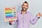 Young hispanic man holding traditional abacus screaming proud, celebrating victory and success very excited with raised arm