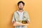 Young hispanic man holding tray with breakfast food puffing cheeks with funny face