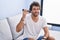 Young hispanic man listening voice message by smartphone sitting on sofa at home