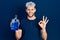 Young hispanic man with modern dyed hair holding mouthwash for fresh breath doing ok sign with fingers, smiling friendly gesturing