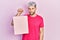 Young hispanic man with modern dyed hair holding shopping bag thinking attitude and sober expression looking self confident