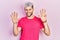 Young hispanic man with modern dyed hair wearing casual pink t shirt showing and pointing up with fingers number nine while