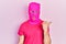 Young hispanic man with modern dyed hair wearing pink balaclava mask face pointing thumb up to the side smiling happy with open