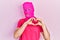 Young hispanic man with modern dyed hair wearing pink balaclava mask face smiling in love doing heart symbol shape with hands