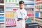 Young hispanic man pharmacist using touchpad holding gel hands bottle at pharmacy