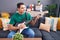 Young hispanic man playing electrical guitar sitting on sofa at home