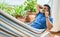 Young hispanic man relaxed talking on the smartphone lying on the hammock at terrace