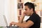 Young hispanic man sitting at desk working on white laptop, profile angle