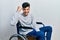 Young hispanic man sitting on wheelchair angry and mad raising fist frustrated and furious while shouting with anger