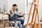 Young hispanic man sitting on wheelchair painting at art studio pointing displeased and frustrated to the camera, angry and