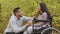 Young hispanic man squatting talking to girl in wheelchair holding hands couple in love relaxing in nature guy visiting