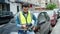 Young hispanic man standing by car wearing reflective vest using smartphone at street