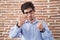 Young hispanic man standing over brick wall background punching fist to fight, aggressive and angry attack, threat and violence