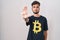 Young hispanic man with tattoos wearing bitcoin t shirt doing stop sing with palm of the hand