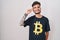 Young hispanic man with tattoos wearing bitcoin t shirt smiling pointing to head with one finger, great idea or thought, good