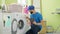 Young hispanic man technician repairing washing machine holding touchpad at laundry room