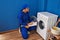 Young hispanic man technician repairing washing machine writing on document at laundry room