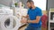 Young hispanic man washing clothes holding dirty at laundry room