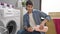 Young hispanic man washing clothes pouring detergent smiling at laundry room