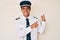 Young hispanic man wearing airplane pilot uniform pointing to the back behind with hand and thumbs up, smiling confident