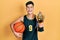 Young hispanic man wearing basketball uniform holding ball and prize celebrating crazy and amazed for success with open eyes