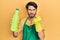Young hispanic man wearing cleaner apron holding cleaning product annoyed and frustrated shouting with anger, yelling crazy with