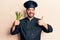 Young hispanic man wearing cooker uniform holding asparagus smiling happy and positive, thumb up doing excellent and approval sign