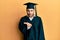 Young hispanic man wearing graduation cap and ceremony robe looking at the camera blowing a kiss with hand on air being lovely and